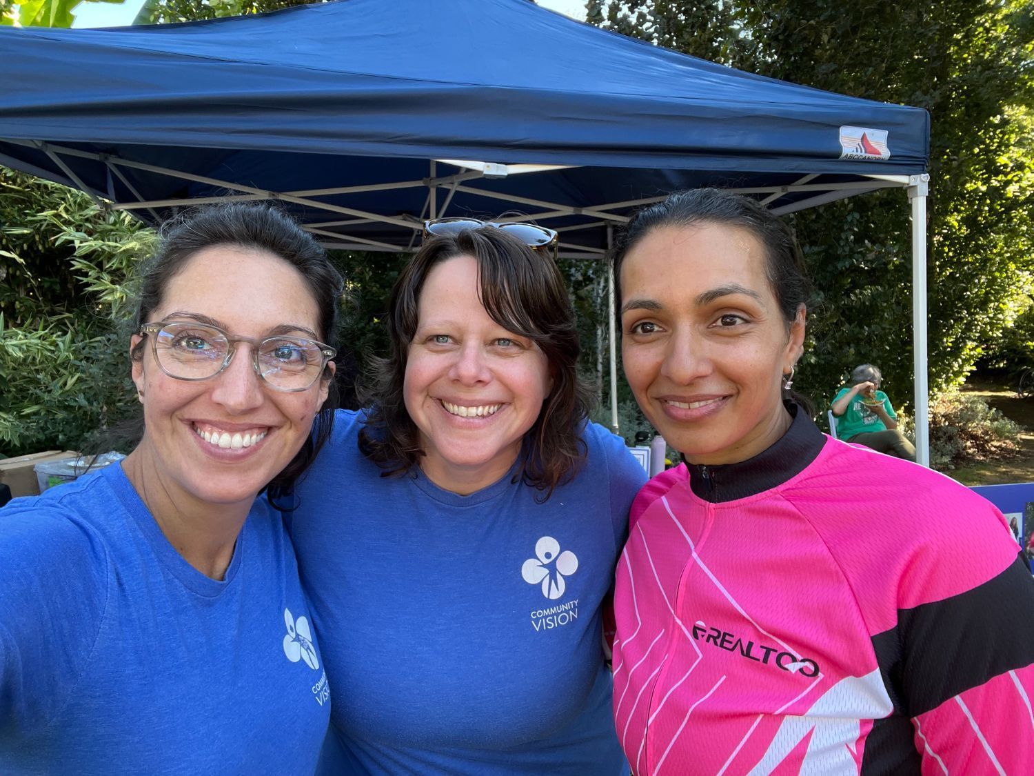 Three women smiling wearing Community Vision shirts.
